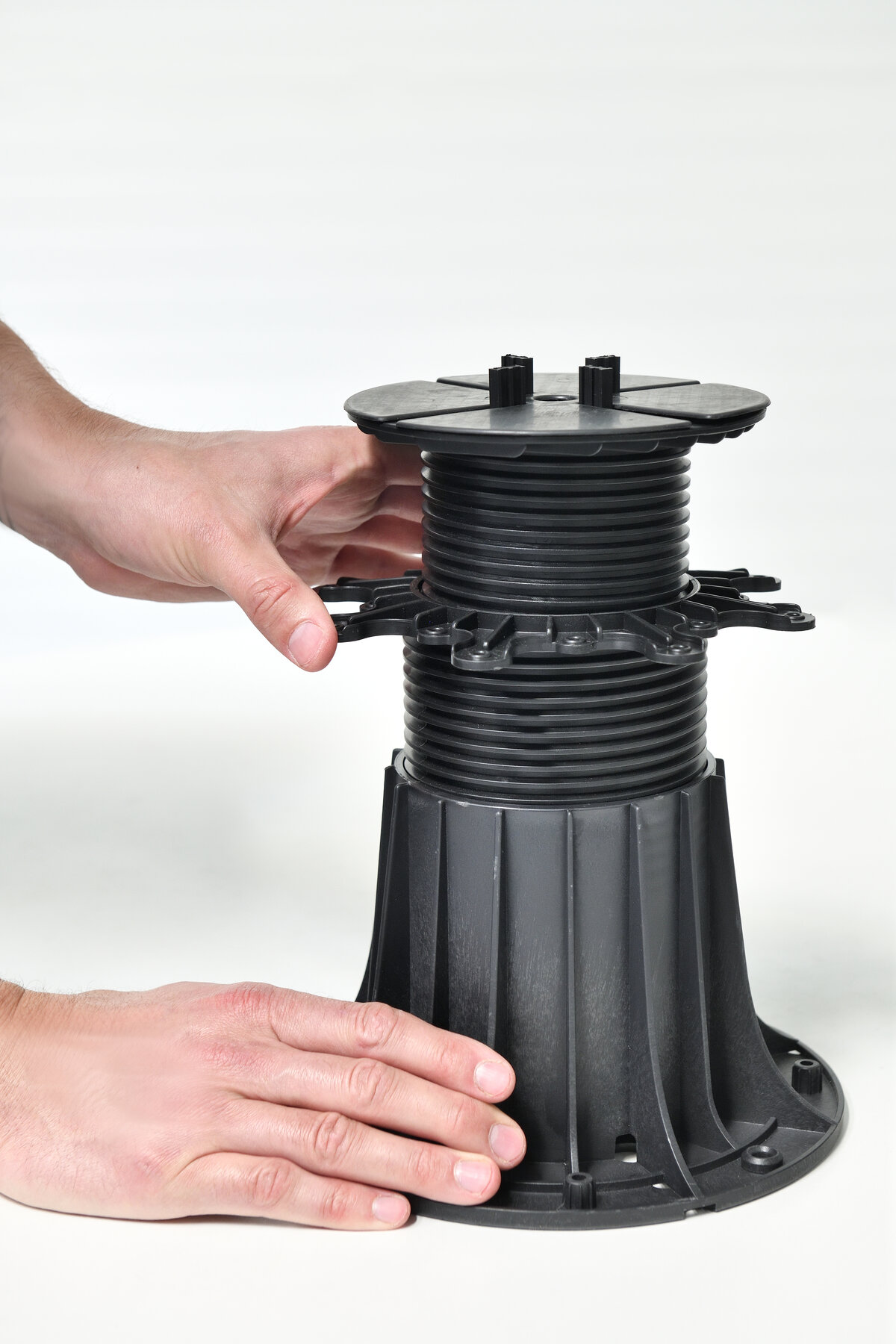 Hands adjusting the height of a black plastic pedestal support for paving tiles.