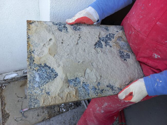 Worker holding a damaged granite paver tile with adhesive mortar residue on the back.