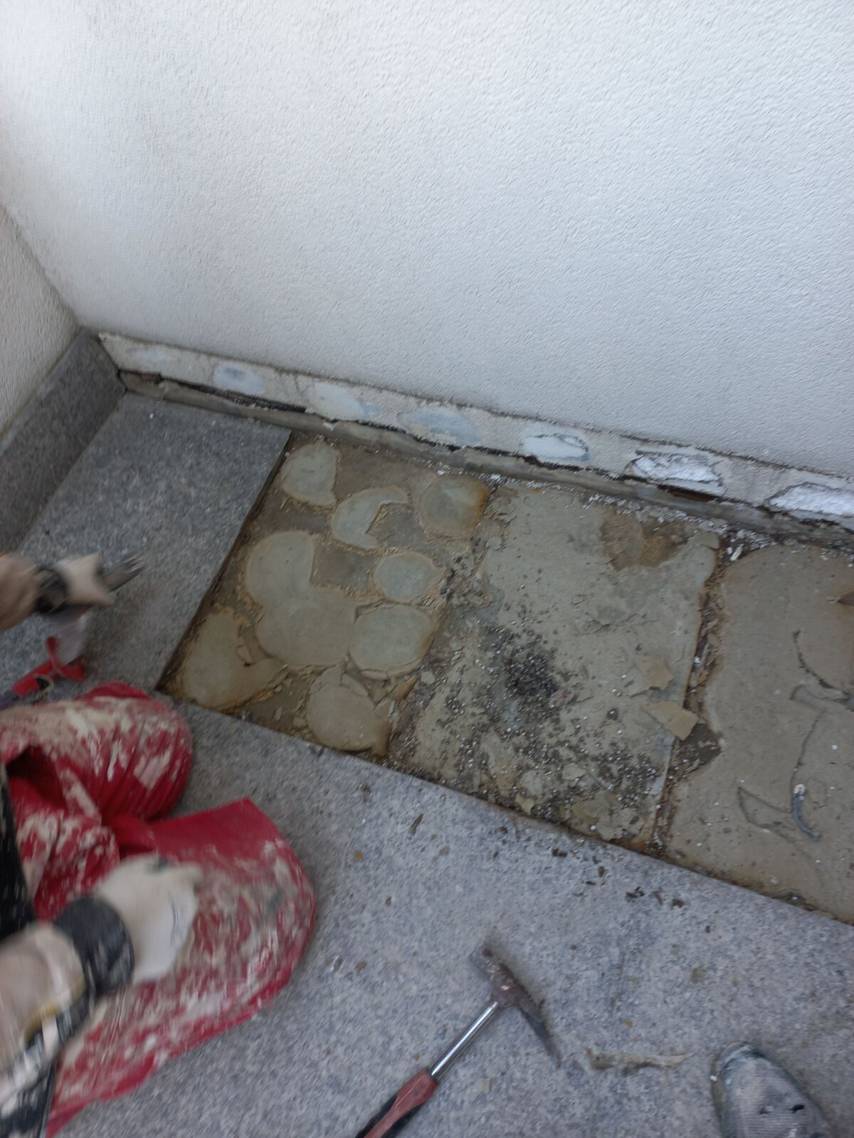 Worker removing damaged stone pavers and adhesive mortar during patio repairs.