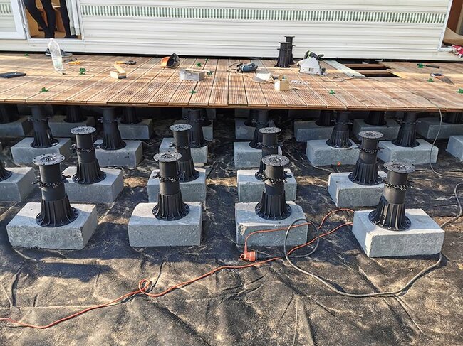 Adjustable deck pedestals mounted on concrete blocks supporting a wooden deck structure.