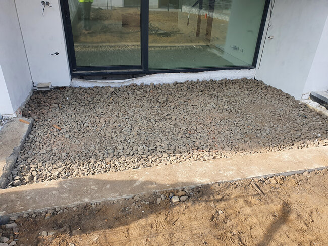 Crushed stone base layer prepared for patio construction outside a sliding glass door.