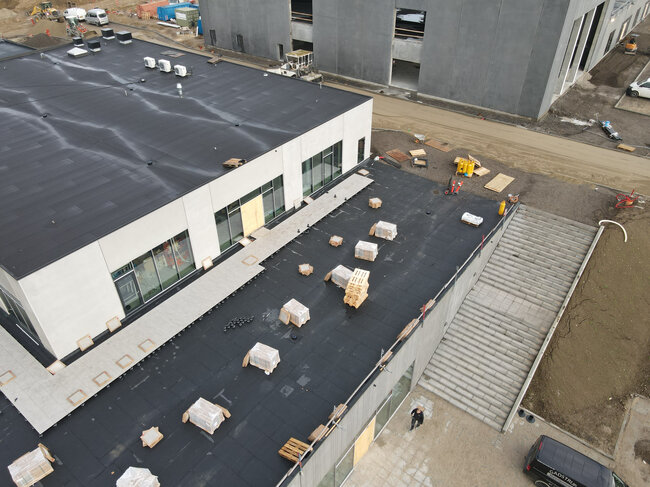Aerial view of building flat roof under construction with paving tiles and pedestals being installed.