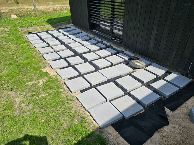 Square concrete pavers arranged on weed barrier fabric for outdoor terrace base preparation.