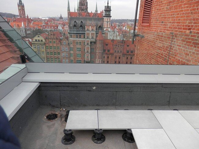 Installation of raised paving tiles supported by adjustable plastic pedestals on a rooftop deck.