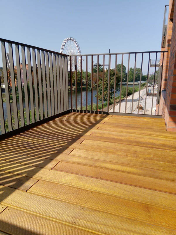 Wooden decking installed on an adjustable pedestal support system on a modern balcony overlooking a river.