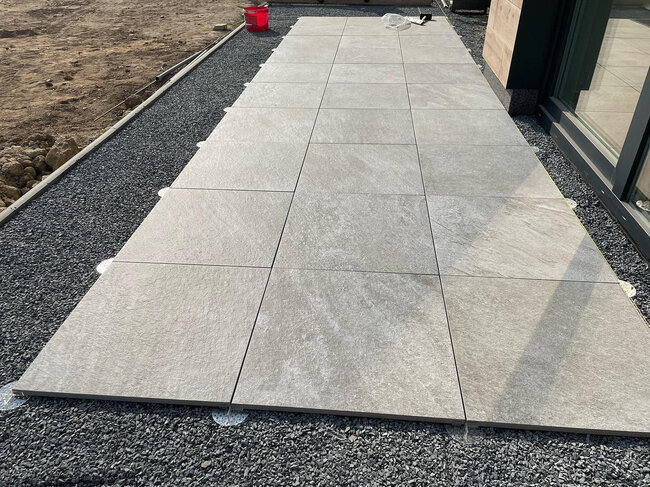 Light grey porcelain pavers installed on low-height adjustable pedestal supports over a gravel base.