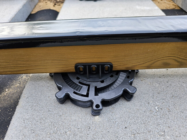 Close-up of an adjustable plastic pedestal supporting a wooden deck joist.