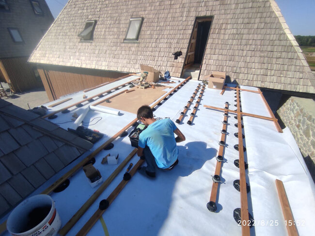 Contractor installing adjustable deck pedestals and wooden joists on a flat roof membrane.