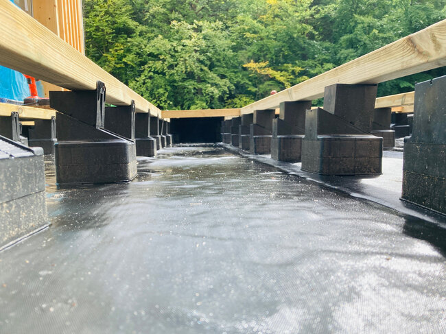 Adjustable plastic deck pedestals supporting wood joists over waterproof roof membrane.