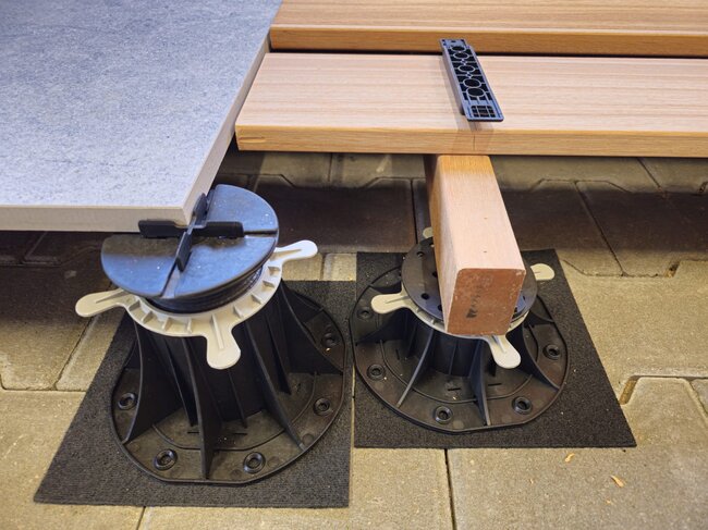 Adjustable pedestals supporting outdoor porcelain paving tile and timber decking joist.
