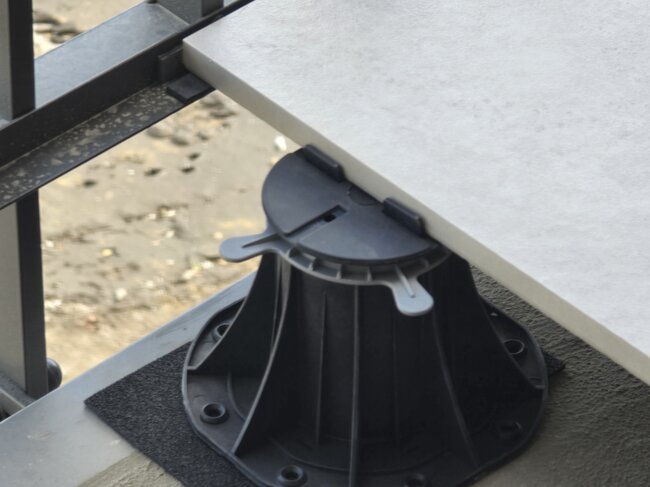 Adjustable pedestal supporting the edge of an outdoor porcelain paving slab on a balcony.