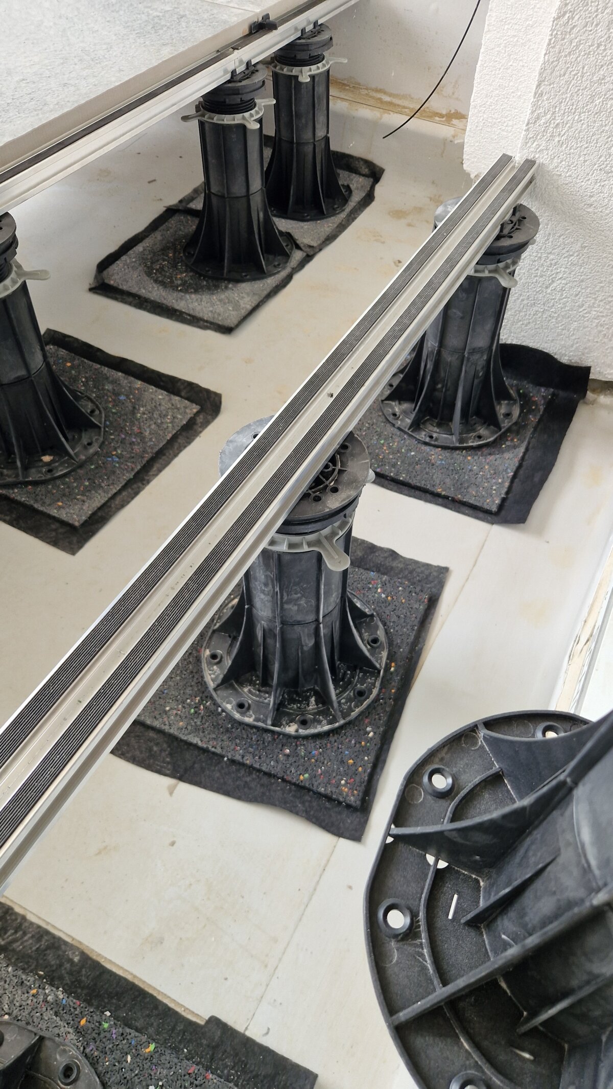 Adjustable pedestals on rubber pads supporting an aluminum decking joist rail for a raised terrace installation.