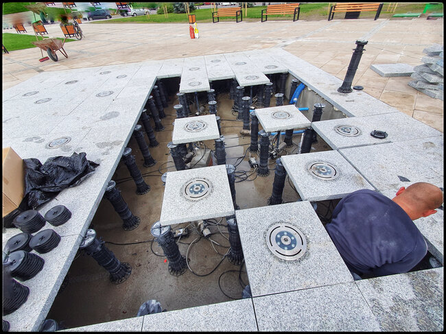 Installing adjustable pedestals and pavers with integrated water jets for an outdoor dry deck fountain system.